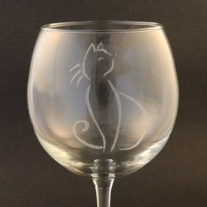 May include: A clear glass wine glass with a delicate etched design of a cat sitting on the side of the glass.