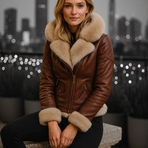 Puede incluir: Chaqueta de cuero marrón con cuello y puños de piel beige. La chaqueta tiene cierre de cremallera y dos bolsillos delanteros. La persona lleva pantalones negros. El fondo es un paisaje urbano borroso.