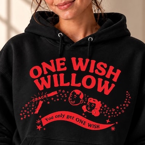 May include: A black hooded sweatshirt featuring a red graphic print on the chest. The text reads ONE WISH WILLOW and You only get ONE WISH, accompanied by illustrations of two faces, a crackling effect, and small stars.
