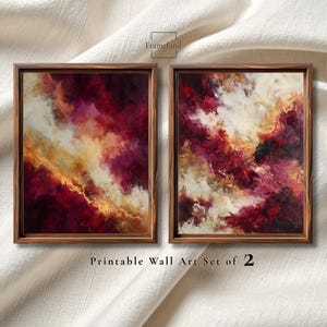 May include: Two framed abstract art prints. The artwork features a blend of burgundy, gold, and white hues, creating a cloud-like effect. The frames are a dark wood. The text at the bottom reads "Printable Wall Art Set of 2".