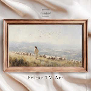 Può includere: Un dipinto di paesaggio incorniciato raffigura una figura in una veste bianca con un gregge di pecore, sullo sfondo di un paesaggio montuoso. L'opera d'arte è in una cornice di legno. I testi "Frameland" e "Frame TV Art" sono visibili.