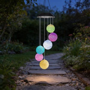 Könnte beinhalten: Solarbetriebener Windspiel mit sieben bunten Glaskugeln, die von einem schwarzen Aufsatz hängen. Die Kugeln in Grün, Lila, Weiß, Blau, Rosa und Gelb hängen in einem Garten mit einem Steinweg. Für den Außenbereich geeignet.