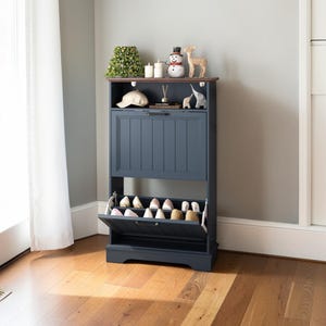 May include: A navy blue shoe storage cabinet with a flip-down door and a top shelf. The cabinet has a dark brown top and is decorated with small figurines and candles. The bottom door is open, revealing several pairs of shoes.