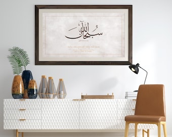May include: A framed artwork featuring Arabic calligraphy in brown script. The artwork is displayed above a white cabinet with decorative vases and candles. A brown leather chair and a black desk lamp are also in the room.