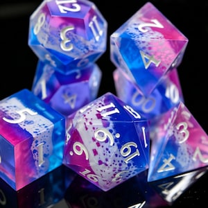 May include: A set of polyhedral dice featuring a translucent blend of blue, purple, and pink colors with white, cloud-like inclusions and splattered patterns. Each die has engraved numbers filled with a metallic silver finish.