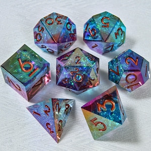 Könnte beinhalten: Eine Sammlung von sieben schillernden, polyedrischen Würfeln in verschiedenen Formen, darunter ein W4, W6, W8, W10, W12, W20 und ein Prozentwürfel. Die Würfel haben einen schimmernden, mehrfarbigen Effekt mit roten Zahlen, ideal für Tabletop-Spiele.