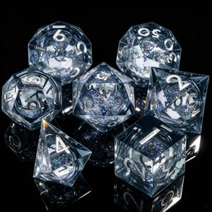 May include: A collection of seven clear, multi-faceted dice with silver numerals and iridescent glitter. The dice are displayed on a reflective black surface. The set includes a d4, d6, d8, d10, d12, d20, and a percentile die, each with a unique geometric shape.