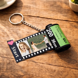 May include: A personalized film roll keychain with a silver chain and ring. The film strip displays two photos and the word "Start" with a pink heart. The film canister is green and black, with text indicating it's 35mm film.