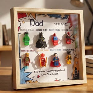 May include: A framed artwork featuring Lego superhero figures. The text reads "Dad, You Are..." followed by various comparisons. The bottom reads "You are our favorite superhero! Love, Alice, Joseph."