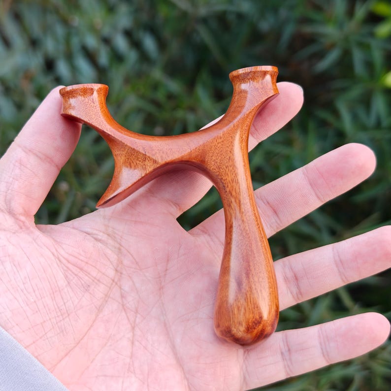 May include: A handcrafted wooden slingshot with a polished finish. The slingshot features a Y-shaped frame with rounded edges and a smooth, ergonomic handle. The wood grain is visible, showcasing the natural color and texture of the material.