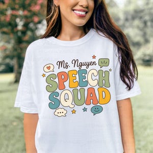 May include: A white short-sleeve t-shirt featuring the text Ms. Nguyen SPEECH SQUAD in colorful, retro-style bubble letters. The design includes various speech bubbles, small stars, and a heart icon in shades of orange, green, blue, and yellow.