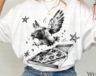 May include: A white short-sleeve t-shirt featuring a black ink-style graphic of a pigeon flying above an open pizza box. The design includes scattered star shapes surrounding the bird. The shirt is paired with blue denim jeans and black sneakers.