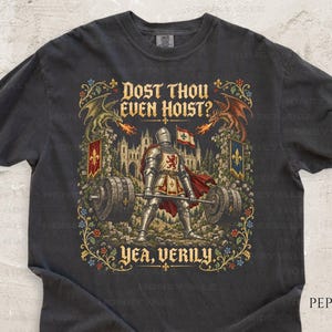 May include: A charcoal grey t-shirt featuring a graphic of a knight in full armour lifting a heavy barbell. The design includes two dragons, a castle, and the text "DOST THOU EVEN HOIST?" at the top and "YEA, VERILY." at the bottom, framed by floral motifs.