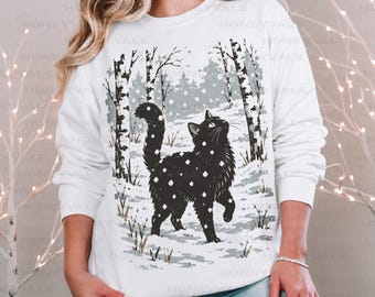 May include: A white long-sleeve sweatshirt featuring a graphic of a black cat standing in a snowy forest with birch trees. The text Gildan 18000 WHITE is printed in the upper right corner. The design shows a cat covered in snowflakes.