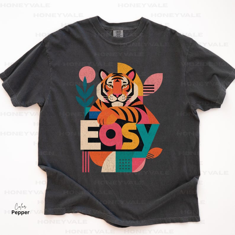 Pode incluir: Uma t-shirt de manga curta cinzento-carv&atilde;o com um gr&aacute;fico de um tigre e formas geom&eacute;tricas em rosa, laranja, azul-petr&oacute;leo e creme. A palavra "Easy" est&aacute; impressa em letras grandes, negrito e multicoloridas no centro da ilustra&ccedil;&atilde;o.