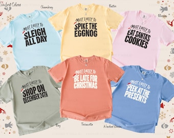 May include: A collection of six short-sleeved crew neck t-shirts in chambray, butter, blossom, bay, terracotta, and washed denim. Each shirt features a unique Christmas-themed graphic with text including Most Likely To Sleigh All Day, Spike The Eggnog, Eat Santa's Cookies, Shop On December 24th, Be Late For Christmas, and Peek At The Presents.
