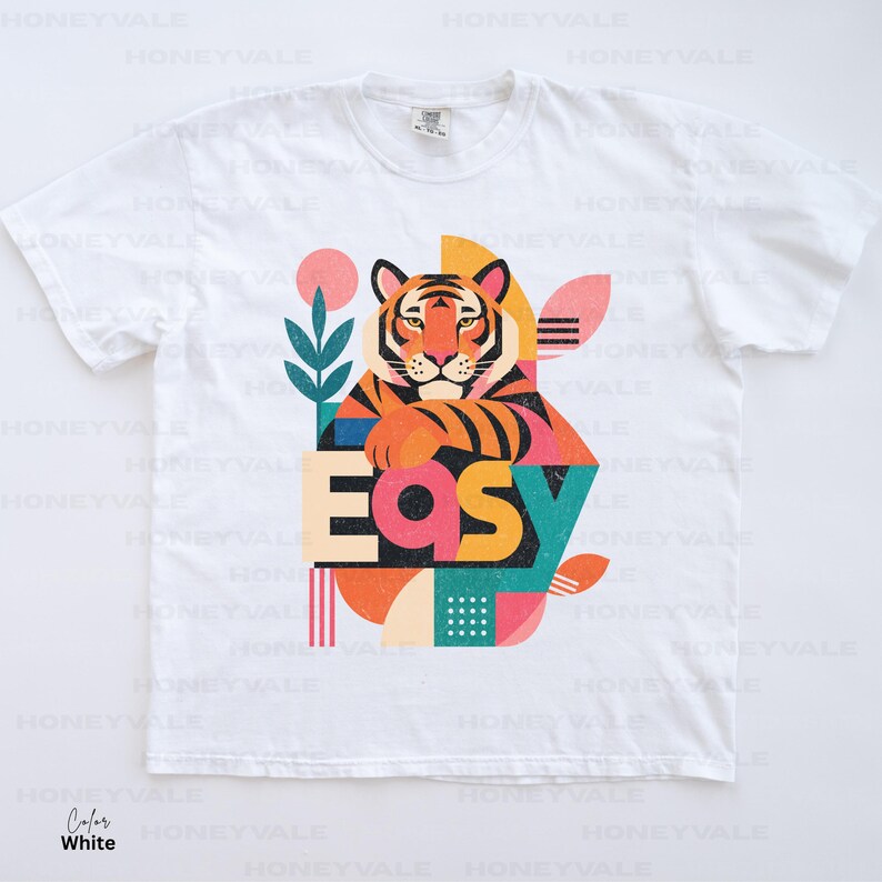 Pode incluir: Uma t-shirt branca de manga curta com uma estampa gr&aacute;fica de um tigre apoiando as patas na palavra "EASY" em letras grandes e coloridas. O design inclui formas geom&eacute;tricas, um c&iacute;rculo rosa e folhas em tom verde-azulado.