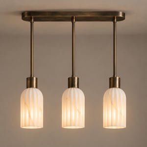 May include: A three-light pendant fixture featuring a rectangular bronze ceiling canopy with three vertical rods supporting cylindrical, fluted white glass shades. Each shade has a subtle marbled texture and is capped with a bronze metal fitting.