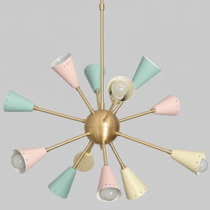 Puede incluir: Una l&aacute;mpara de ara&ntilde;a de estilo retro con una esfera central de lat&oacute;n y m&uacute;ltiples brazos. Cada brazo sostiene una pantalla c&oacute;nica en tonos pastel, rosa, verde menta y amarillo. Las l&aacute;mparas tienen peque&ntilde;os agujeros en el borde.