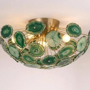 May include: A unique ceiling light fixture featuring green agate slices arranged around a central light source. The fixture has a gold-colored metal frame with multiple light bulbs. The agate slices vary in shade from light to dark green.