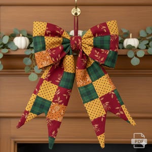 May include: A large, decorative bow with a patchwork design in fall colors. The bow features squares of yellow polka dots, green plaid, and burgundy fabric with leaf patterns. It hangs from a gold hook, perfect for seasonal decor.