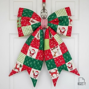 May include: A large, quilted Christmas bow in red, green, and white, hanging on a white door. The bow features a patchwork design with Santa Claus, reindeer, and Christmas tree motifs. The bow is attached to a metal hook with a red ribbon.