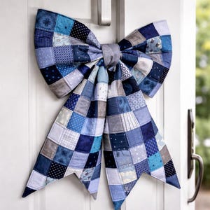 Könnte beinhalten: Eine große, dekorative Schleife aus gestepptem Stoff mit einem Patchwork-Design in Blau-, Grau- und Weißtönen. Die Schleife ist an einer weißen Tür befestigt, mit einem silbernen Griff. Das Design der Schleife umfasst verschiedene Muster.