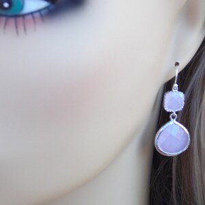 May include: Silver dangle earrings with two light pink faceted stones. The larger stone is teardrop shaped and the smaller stone is square shaped.