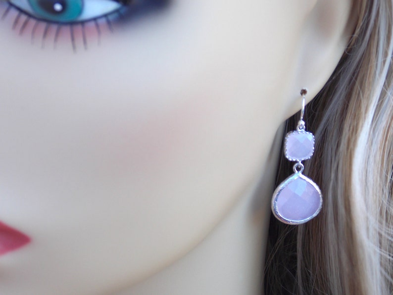 May include: Silver dangle earrings with two light pink faceted stones. The larger stone is teardrop shaped and the smaller stone is square shaped.