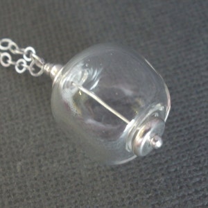 May include: A silver chain necklace with a clear glass orb pendant containing a silver wire. The orb is attached to the chain with a silver clasp.