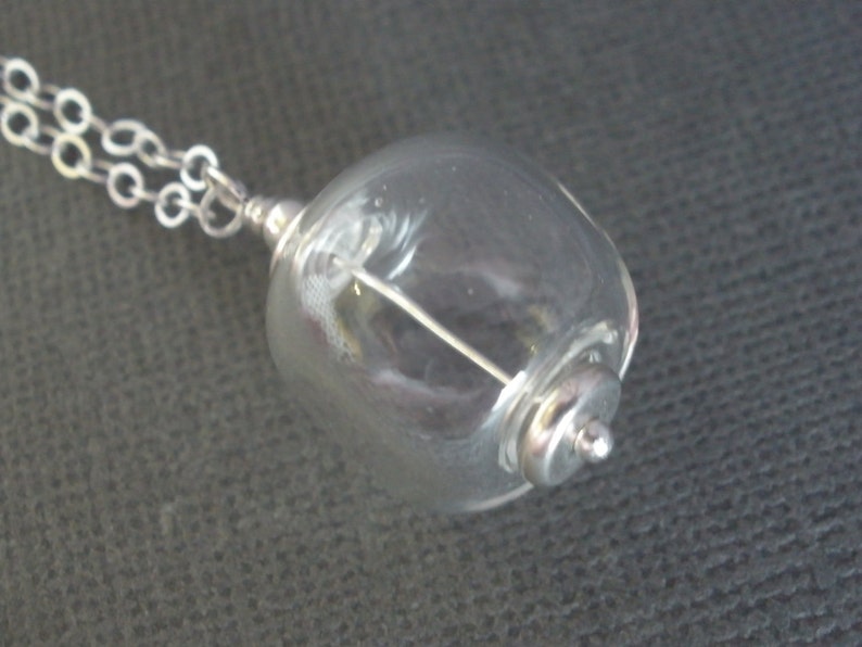 May include: A silver chain necklace with a clear glass orb pendant containing a silver wire. The orb is attached to the chain with a silver clasp.