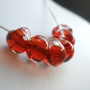 May include: A silver chain necklace with a series of red glass beads. The beads are round and have a translucent quality, with some showing a hint of white inside.