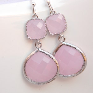 May include: A pair of silver dangle earrings with two pink faceted glass stones on each earring. The top stone is square and the bottom stone is teardrop shaped.