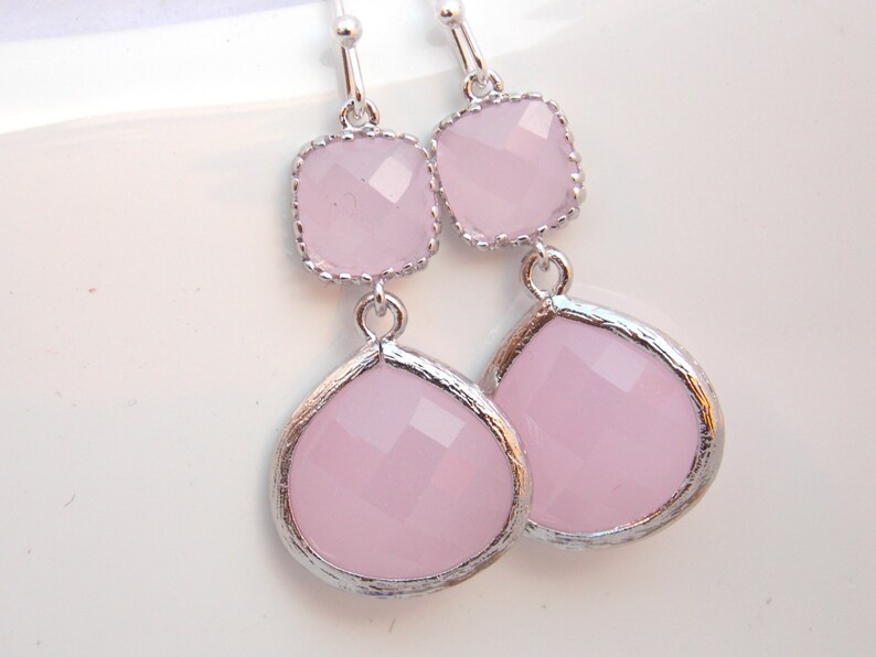 May include: A pair of silver dangle earrings with two pink faceted glass stones on each earring. The top stone is square and the bottom stone is teardrop shaped.