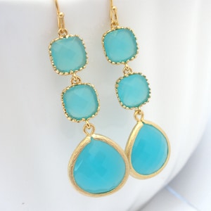 May include: Gold dangle earrings with three turquoise blue square-shaped stones and a teardrop-shaped stone.