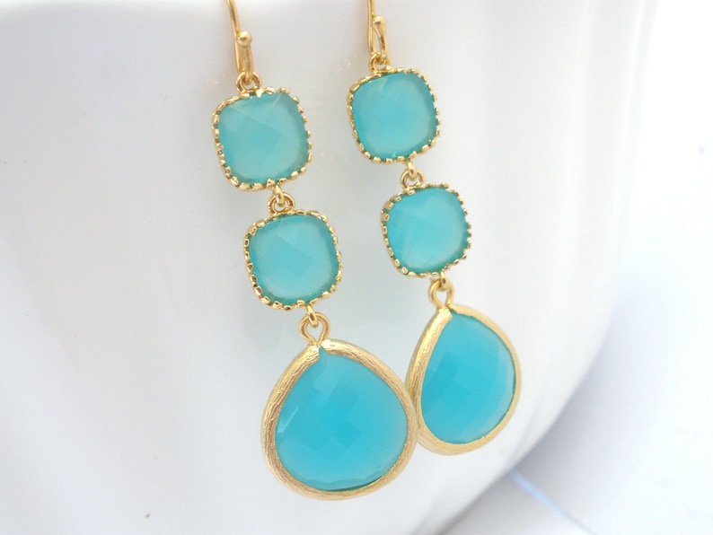May include: Gold dangle earrings with three turquoise blue square-shaped stones and a teardrop-shaped stone.