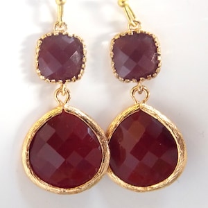 May include: A pair of gold tone dangle earrings with two burgundy colored faceted glass stones on each earring.