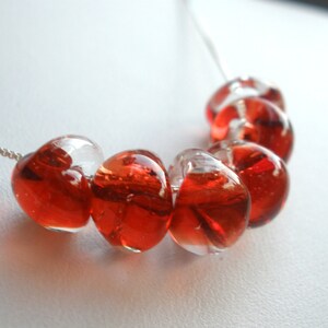 May include: A silver chain necklace with red glass heart-shaped beads. The beads are clear with red swirls inside.