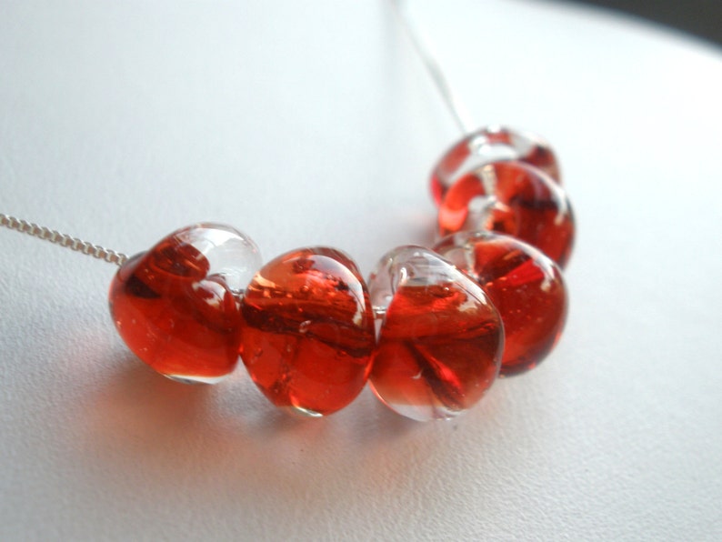 May include: A silver chain necklace with red glass heart-shaped beads. The beads are clear with red swirls inside.
