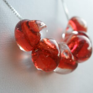 May include: A necklace with a silver chain and red glass beads. The beads are round and have a clear, translucent quality.