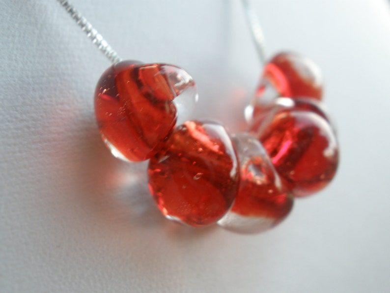 May include: A necklace with a silver chain and red glass beads. The beads are round and have a clear, translucent quality.