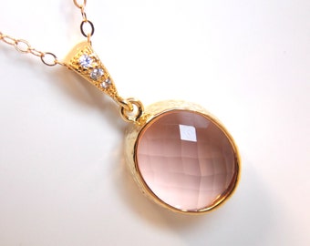 May include: A gold chain necklace with a pink oval pendant featuring a faceted gemstone and small clear stones.