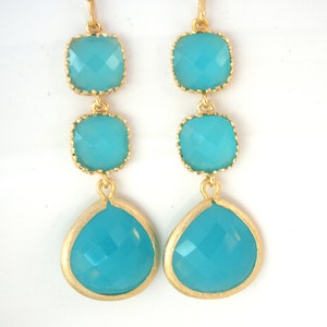 May include: Gold earrings with three turquoise blue gemstone drops. The top two gemstones are square and the bottom gemstone is teardrop shaped.