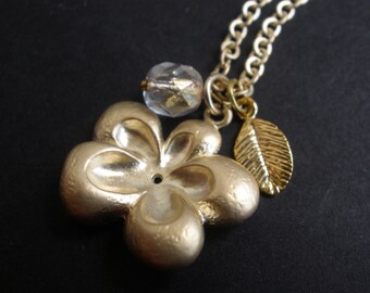 May include: Gold necklace with a flower charm, a crystal bead, and a leaf charm.