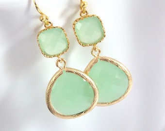 Puede incluir: Pendientes de tono dorado con dos piedras de vidrio verde claro en forma de lágrima y dos piedras de vidrio verde claro en forma cuadrada.
