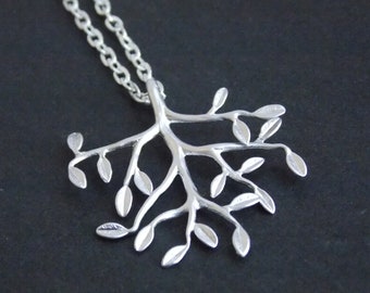 Puede incluir: Un collar de plata con un colgante de árbol. El árbol tiene muchas ramas y hojas.