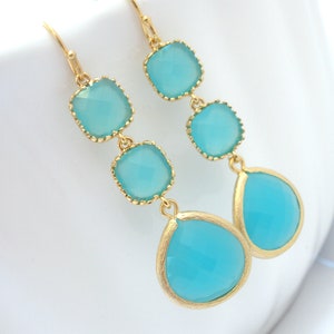 May include: Gold dangle earrings with three turquoise blue square-shaped stones and a teardrop-shaped stone.