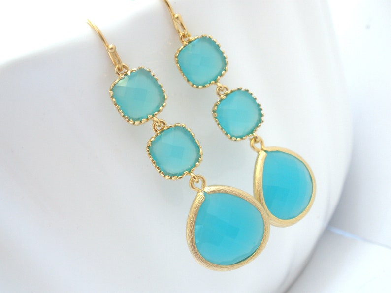 May include: Gold dangle earrings with three turquoise blue square-shaped stones and a teardrop-shaped stone.