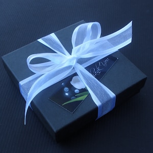 May include: A black gift box tied with a white ribbon and bow. The box has a small card attached with the words "Thank You" written on it.