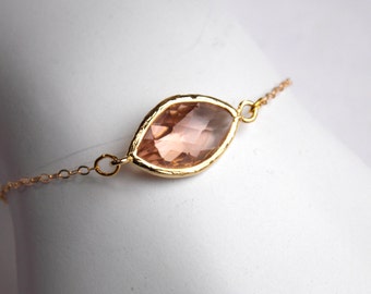 May include: A delicate gold chain bracelet with a single, large, light pink faceted gemstone pendant.